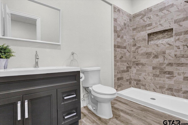 bathroom featuring wood-type flooring, vanity, toilet, and tiled shower