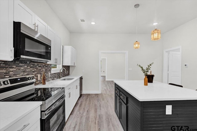 kitchen featuring stainless steel appliances, light hardwood / wood-style floors, white cabinetry, sink, and hanging light fixtures