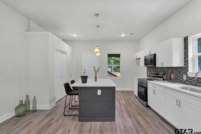 kitchen featuring stainless steel appliances, white cabinetry, sink, light wood-type flooring, and pendant lighting