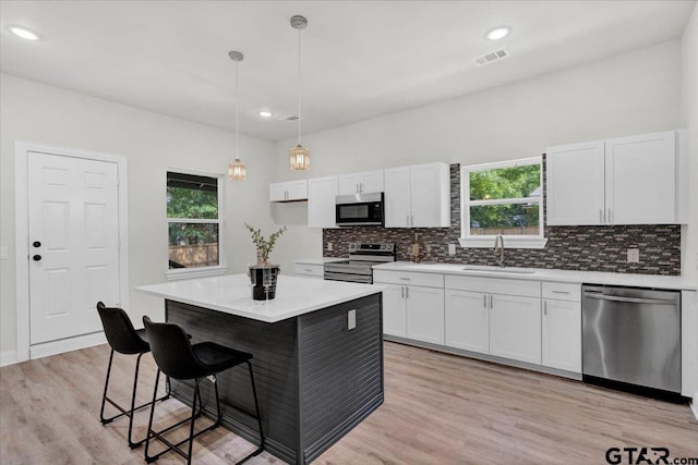 kitchen featuring a center island, appliances with stainless steel finishes, sink, white cabinets, and light hardwood / wood-style flooring