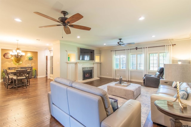 living room featuring a stone fireplace, ceiling fan with notable chandelier, ornamental molding, and hardwood / wood-style floors