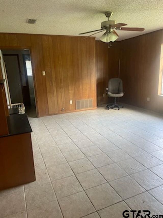 tiled empty room featuring wood walls, a textured ceiling, and ceiling fan