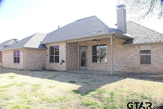 back of house with a shingled roof, brick siding, ceiling fan, and a chimney