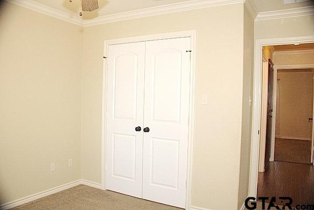 unfurnished bedroom with carpet, crown molding, baseboards, and a closet