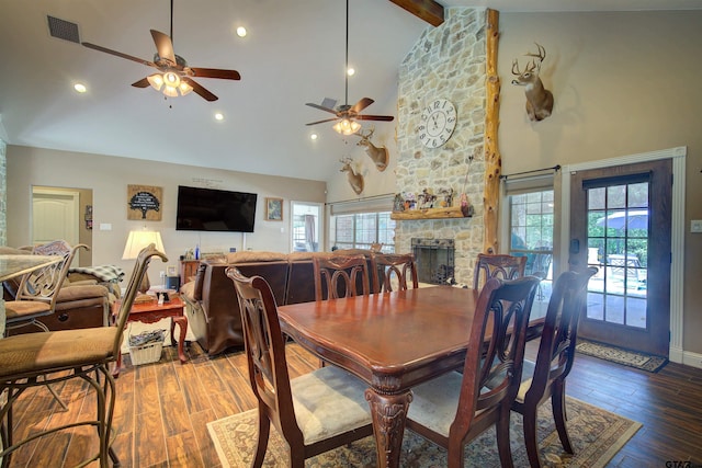 dining area featuring hardwood / wood-style floors, a stone fireplace, ceiling fan, high vaulted ceiling, and beam ceiling