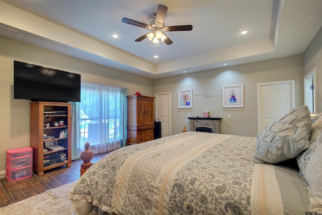 bedroom featuring ceiling fan, a raised ceiling, and a stone fireplace