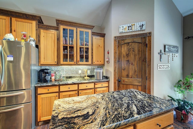 kitchen with backsplash, stainless steel fridge, dark stone counters, and vaulted ceiling