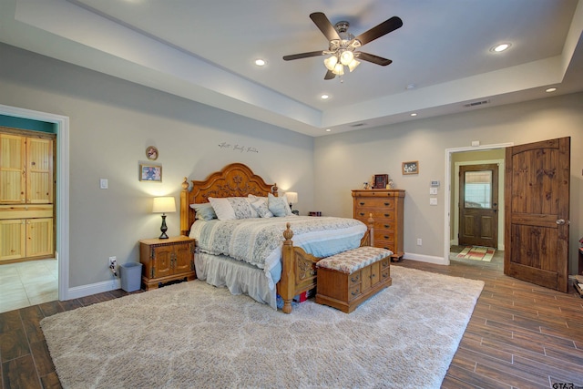 bedroom featuring ceiling fan, a tray ceiling, and ensuite bath