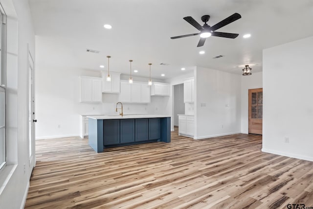 kitchen featuring a kitchen island with sink, pendant lighting, ceiling fan, and light hardwood / wood-style floors