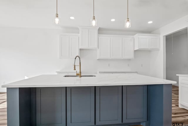 kitchen featuring a large island with sink, white cabinets, light stone countertops, decorative light fixtures, and light hardwood / wood-style floors