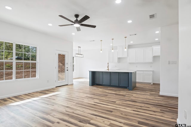 kitchen with ceiling fan, hanging light fixtures, a center island with sink, white cabinets, and light wood-type flooring