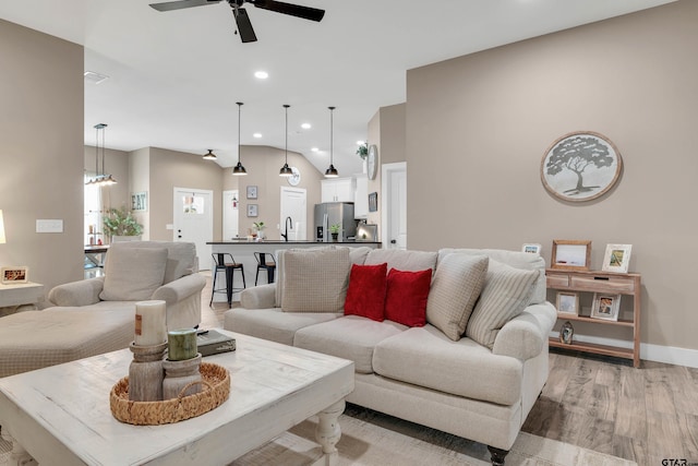 living room with light wood-type flooring, vaulted ceiling, ceiling fan, and sink