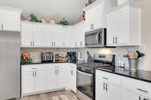 kitchen with decorative backsplash, white cabinets, appliances with stainless steel finishes, and dark stone countertops