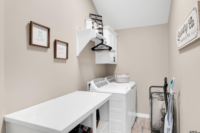 laundry room featuring washing machine and clothes dryer, light hardwood / wood-style flooring, and cabinets