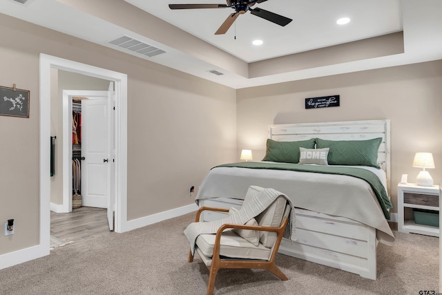 bedroom with ceiling fan, a spacious closet, carpet floors, and a tray ceiling