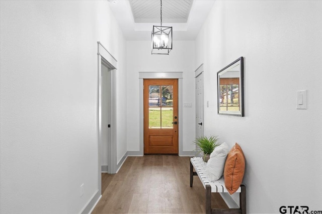 doorway featuring a high ceiling, light wood-type flooring, a tray ceiling, and a notable chandelier