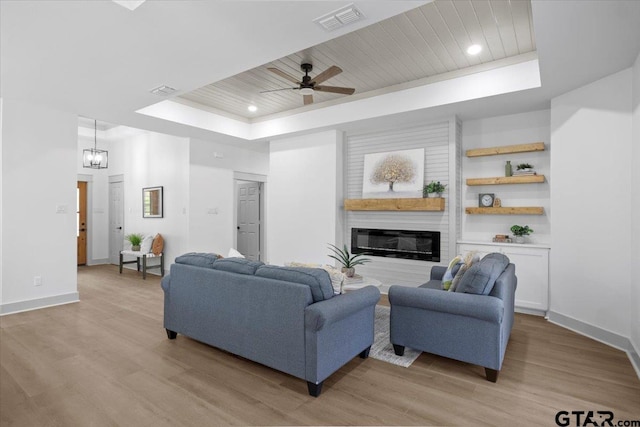 living room with ceiling fan with notable chandelier, a tray ceiling, light hardwood / wood-style flooring, and wooden ceiling