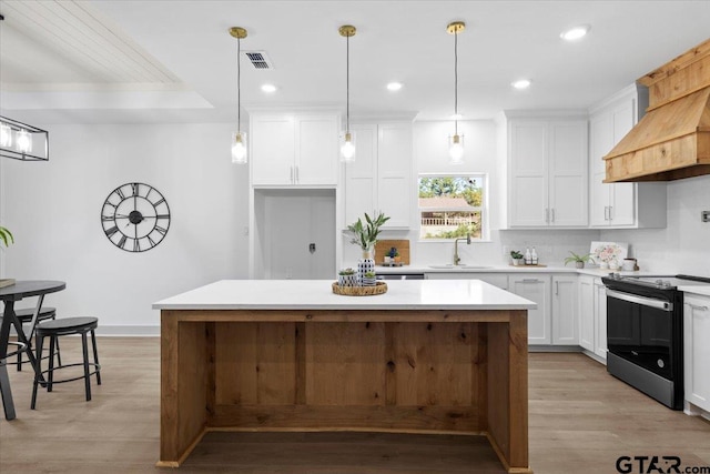 kitchen featuring white cabinetry, electric range, a center island, pendant lighting, and light wood-type flooring