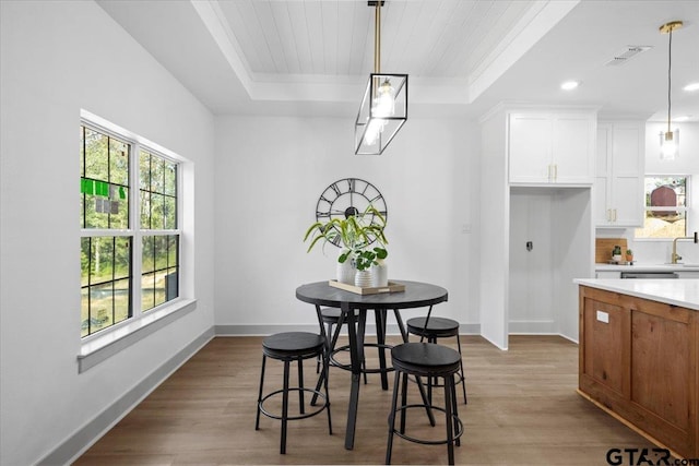 dining space with a raised ceiling, sink, and light hardwood / wood-style flooring