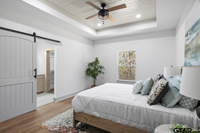 bedroom featuring a barn door, a raised ceiling, light hardwood / wood-style flooring, and ensuite bath