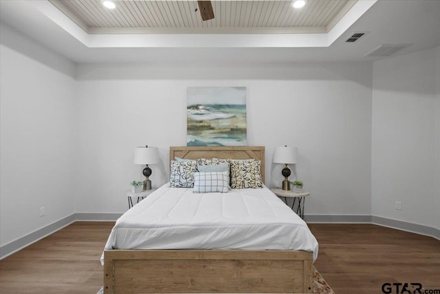 bedroom with wood-type flooring, a tray ceiling, and ceiling fan