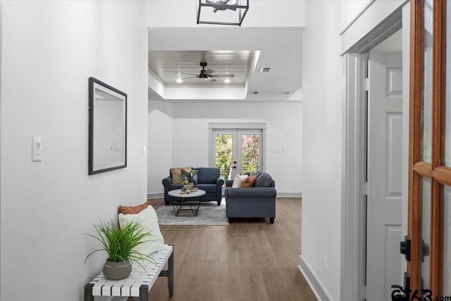 corridor featuring wood-type flooring, a tray ceiling, and french doors