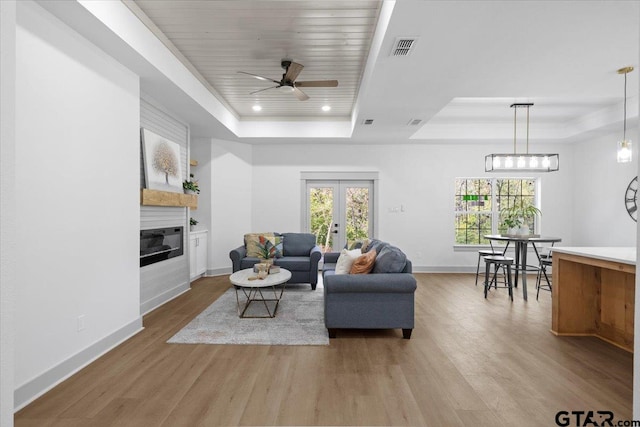 living room with a tray ceiling, ceiling fan, and light hardwood / wood-style flooring