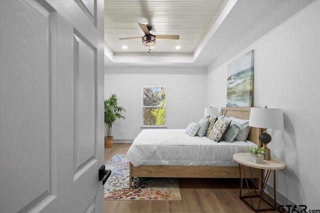 bedroom featuring hardwood / wood-style flooring, ceiling fan, and a tray ceiling