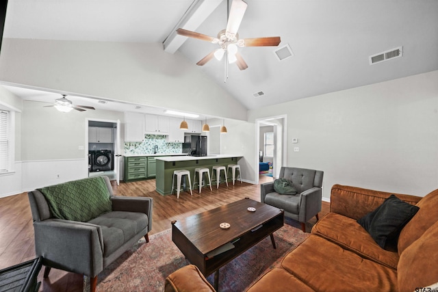 living room featuring washer / clothes dryer, high vaulted ceiling, hardwood / wood-style floors, and beamed ceiling