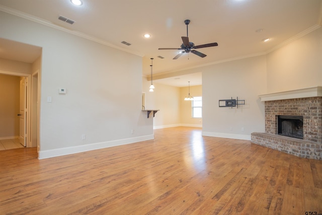 unfurnished living room featuring crown molding, a brick fireplace, ceiling fan with notable chandelier, and light wood-type flooring