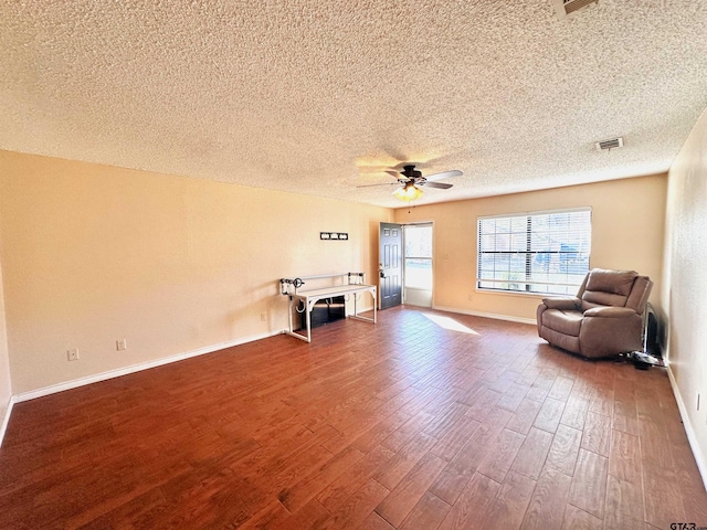 living area featuring dark wood-type flooring, a textured ceiling, and ceiling fan