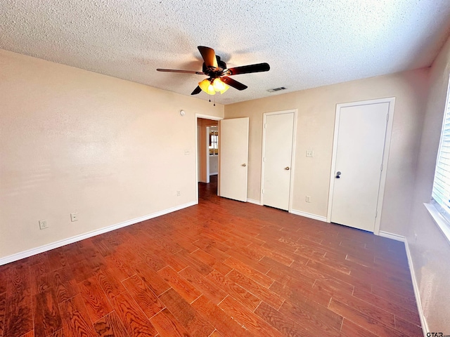 unfurnished bedroom with a textured ceiling, hardwood / wood-style floors, multiple closets, and ceiling fan