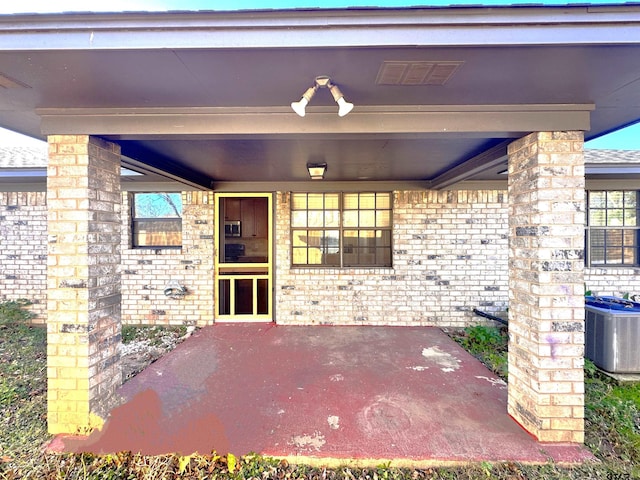 view of exterior entry featuring central AC unit and a patio