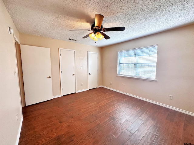 unfurnished bedroom with a textured ceiling, two closets, ceiling fan, and dark hardwood / wood-style floors