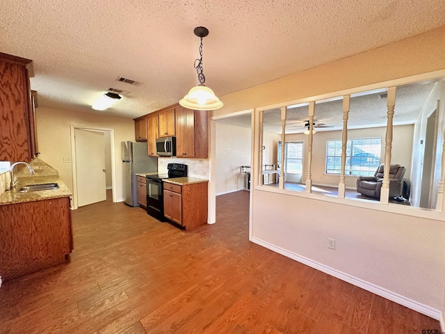 kitchen with stainless steel appliances, a textured ceiling, dark hardwood / wood-style flooring, hanging light fixtures, and sink