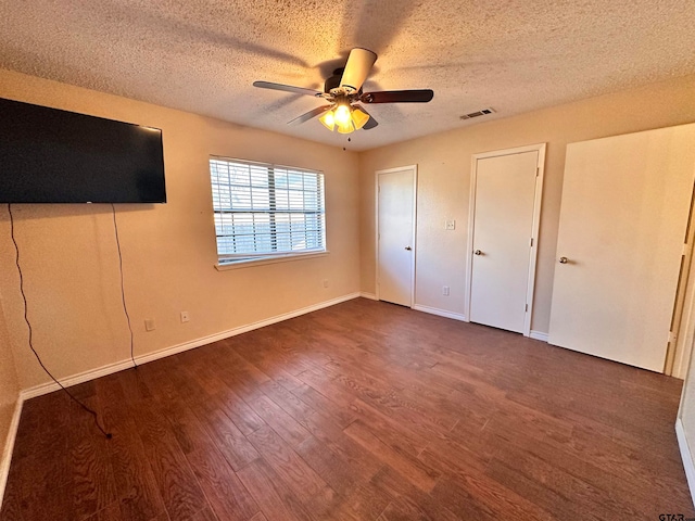 unfurnished bedroom featuring a textured ceiling, dark wood-type flooring, ceiling fan, and two closets