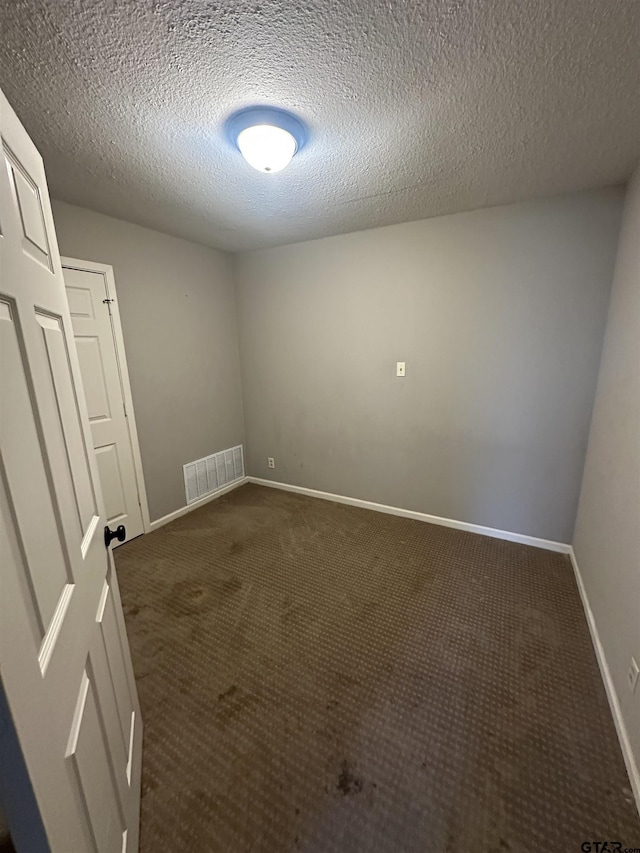 empty room featuring a textured ceiling, dark carpet, visible vents, and baseboards