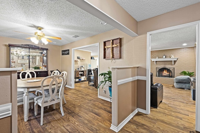 2207 Pinecrest Dr, Gladewater, TX 75647 - dining space with visible vents, ceiling fan, a brick fireplace, and wood finished floors