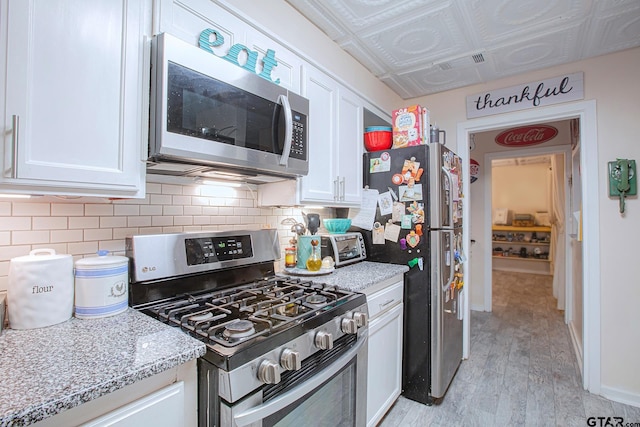 kitchen featuring white cabinets, appliances with stainless steel finishes, light hardwood / wood-style floors, and light stone countertops