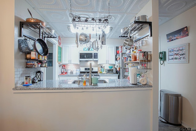 kitchen with tasteful backsplash, light stone counters, stainless steel appliances, sink, and white cabinetry