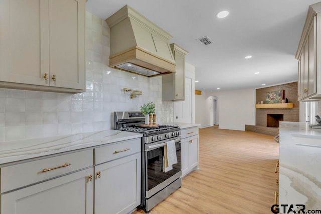 8100 Jewell Ln, Tyler, TX 75703 - kitchen featuring stainless steel gas stove, custom exhaust hood, open floor plan, a fireplace, and decorative backsplash