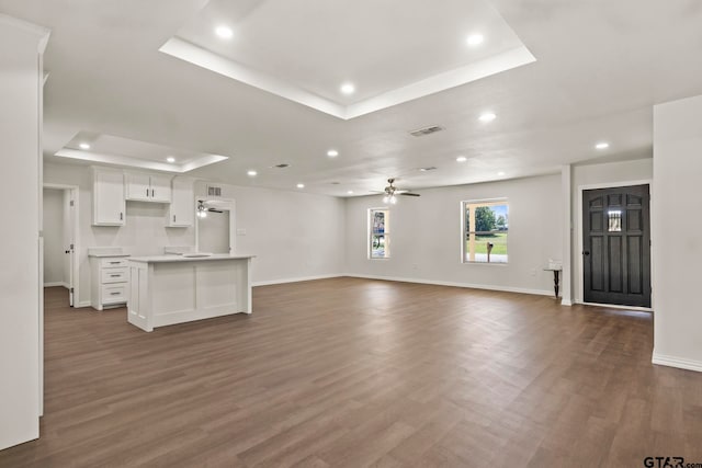 unfurnished living room with ceiling fan, dark wood-type flooring, and a tray ceiling