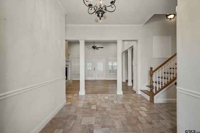 entrance foyer featuring crown molding, ceiling fan with notable chandelier, stone finish flooring, baseboards, and decorative columns