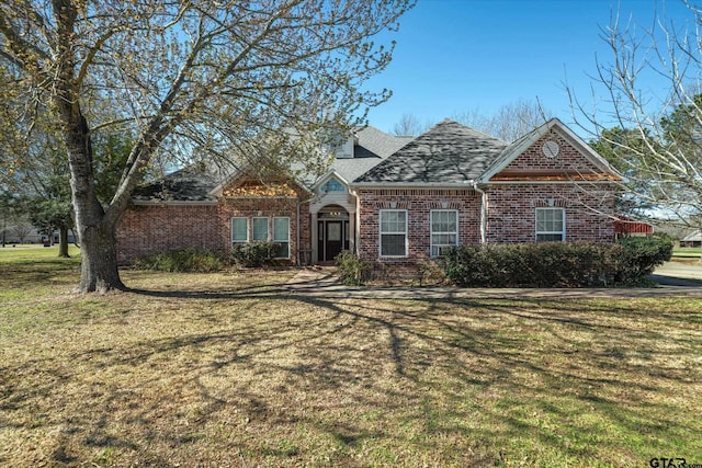 view of front facade with brick siding, roof with shingles, and a front lawn