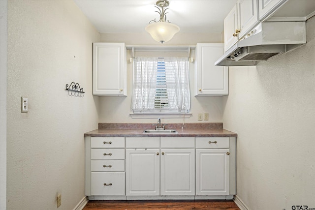 kitchen with dark wood-style floors, a sink, baseboards, white cabinetry, and under cabinet range hood