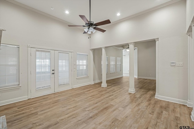 unfurnished living room with a towering ceiling, ornate columns, french doors, light wood-style floors, and ceiling fan