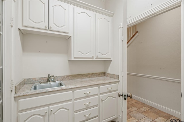 clothes washing area featuring stone finish flooring, baseboards, and a sink