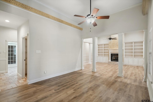 unfurnished living room featuring baseboards, built in shelves, ceiling fan, a fireplace, and ornamental molding