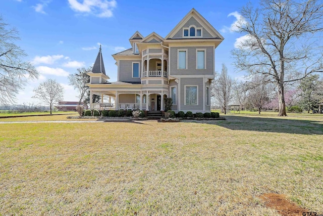 victorian house with a balcony, a front yard, and covered porch