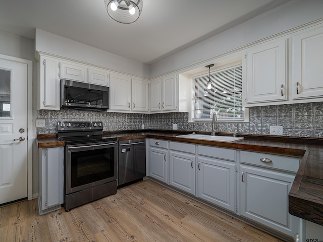 kitchen with a sink, appliances with stainless steel finishes, tasteful backsplash, and butcher block counters